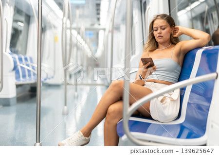 Young woman sitting in subway car with phone Young woman sitting in subway car with phone 139625647