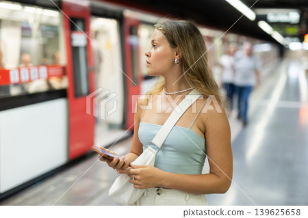 Young girl standing in platform with phone in hand Young girl standing in platform with phone in hand 139625658