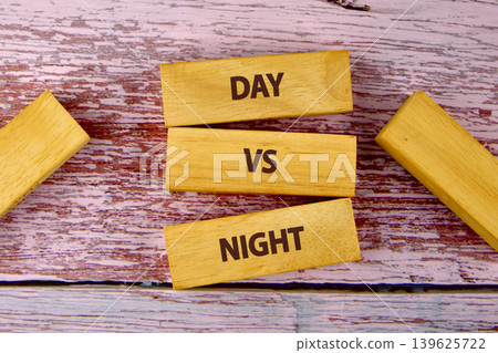 Three wooden blocks spell DAY VS NIGHT, stacked on a faded red and white wooden background. More blocks are scattered, adding to this conceptual representation of comparison Three wooden blocks spell DAY VS NIGHT, stacked on a faded red and white wooden background. More blocks are scattered, adding to this conceptual representation of comparison 139625722