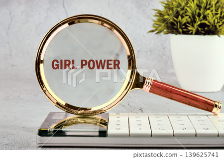 A magnifying glass with a wooden handle rests on a white keyboard. It sharply focuses on the phrase Girl Power. A green potted plant stands in the background on a grey desk A magnifying glass with a wooden handle rests on a white keyboard. It sharply focuses on the phrase Girl Power. A green potted plant stands in the background on a grey desk 139625741