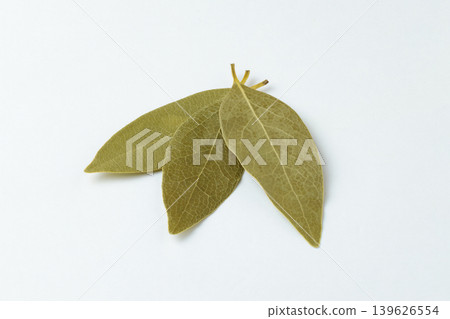 A photograph of three dried bay leaves arranged in a fan shape against a white background. A photograph of three dried bay leaves arranged in a fan shape against a white background. 139626554
