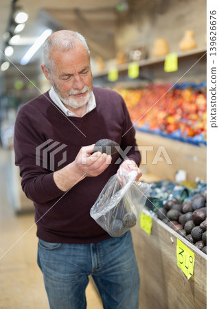 Elderly man shopper choose a ripe avocado against the background of a counter 139626676
