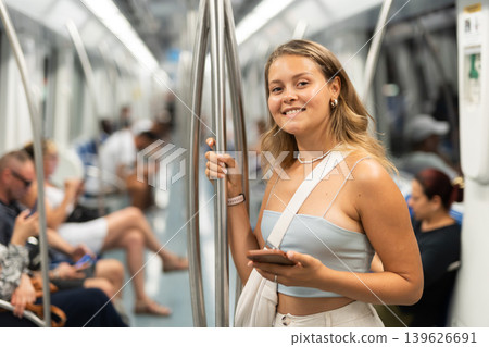Young woman is standing in subway car with phone, getting to work school. Young woman is standing in subway car with phone, getting to work school. 139626691