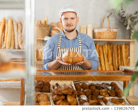 Man seller stands at bakery counter with basket filled with fresh loaf bread. Man seller stands at bakery counter with basket filled with fresh loaf bread. 139626705