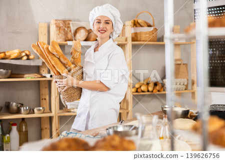 Smiling female baker offering golden crispy baguettes in bakery 139626756