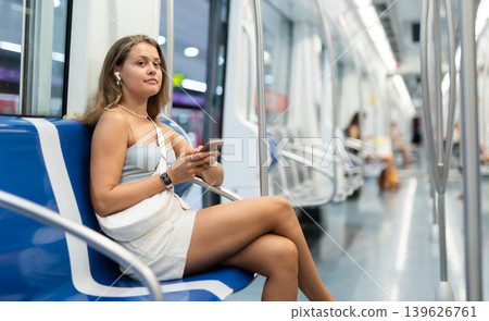 Young girl sitting in wagon holding phone and wireless headphones on airs Young girl sitting in wagon holding phone and wireless headphones on airs 139626761