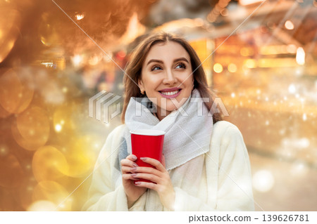 Girl in fur coat stands with glass of coffee in hands on shiny flashing festive sparkling background Girl in fur coat stands with glass of coffee in hands on shiny flashing festive sparkling background 139626781