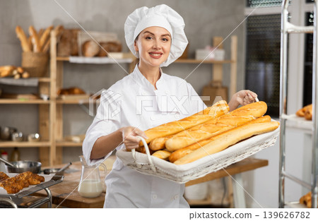 Young female baker with basket of baguettes 139626782
