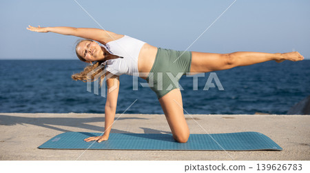 On windy day young slender woman does yoga near sea doing Virabhadrasana On windy day young slender woman does yoga near sea doing Virabhadrasana 139626783