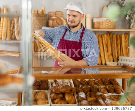 Man seller puts baguettes in paper bag for buyer, packs goods. Man seller puts baguettes in paper bag for buyer, packs goods. 139626787
