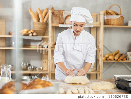 Young female baker kneading dough on table Young female baker kneading dough on table 139626788