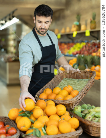 salesman in an apron lays out fresh oranges on the counter salesman in an apron lays out fresh oranges on the counter 139626794