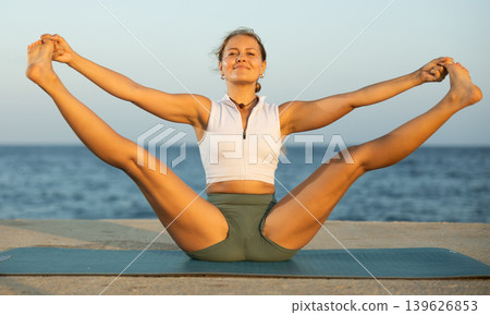 Girl practicing hatha yoga on sea beach, stretching in an asymmetrical seated asana Parivritta Janu Sirsasana Girl practicing hatha yoga on sea beach, stretching in an asymmetrical seated asana Parivritta Janu Sirsasana 139626853