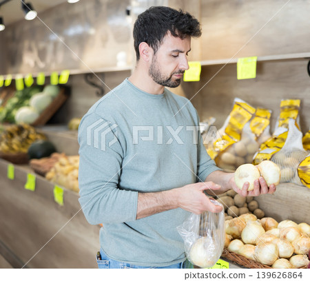 Man chooses ripe onions for purchase in greengrocer shop Man chooses ripe onions for purchase in greengrocer shop 139626864