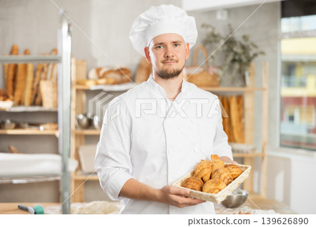 Baker in white uniform stands behind counter in small private bakery offering hot croissants 139626890