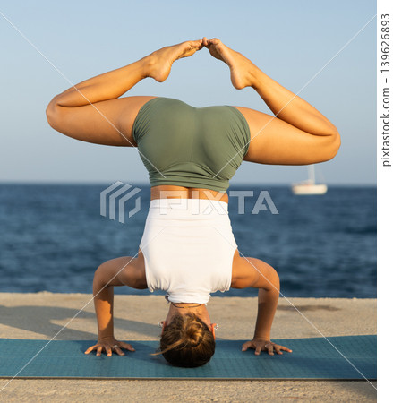 Sportive girl practicing headstand pose of yoga on seashore Sportive girl practicing headstand pose of yoga on seashore 139626893
