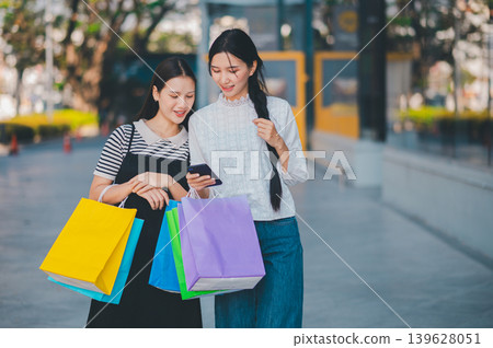 Two women are walking down a street, one of them holding a cell phone Two women are walking down a street, one of them holding a cell phone 139628051
