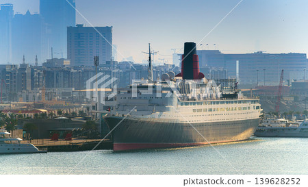 Dubai, United Arab Emirates - Jan 20 2024, panoramic view of the ship Queen Elizabeth II converted by hotel, in port of Dubai, buildings and skyscrapers in background, at morning, Dubai, UAE Dubai, United Arab Emirates - Jan 20 2024, panoramic view of the ship Queen Elizabeth II converted by hotel, in port of Dubai, buildings and skyscrapers in background, at morning, Dubai, UAE 139628252