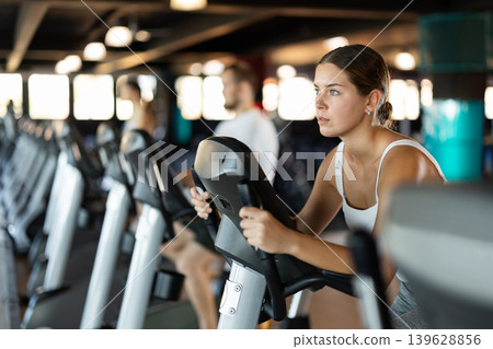 Girl performs exercises with stationary bicycle in gym 139628856