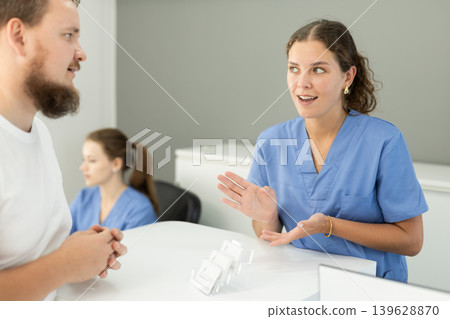 man is standing near the reception in the dentistry and asks about an appointment with a dentist man is standing near the reception in the dentistry and asks about an appointment with a dentist 139628870