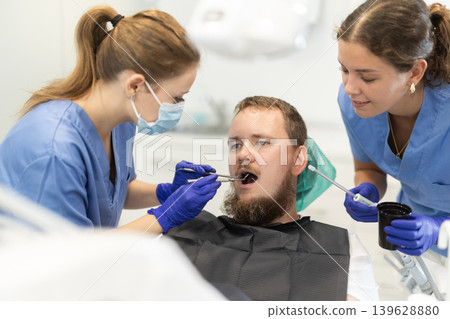 Two women dentists treating a man teeth Two women dentists treating a man teeth 139628880