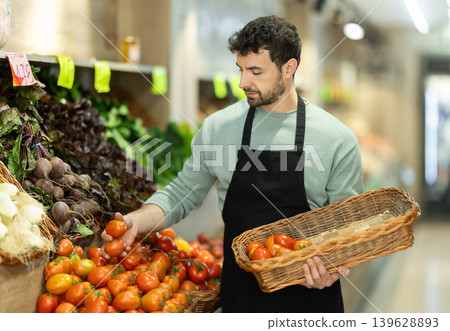 supermarket worker stands with a basket in his hands and lays out farm tomatoes supermarket worker stands with a basket in his hands and lays out farm tomatoes 139628893
