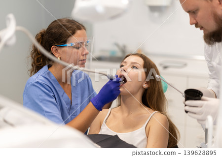 Female dentist treats a client teeth together with an assistant in the office Female dentist treats a client teeth together with an assistant in the office 139628895