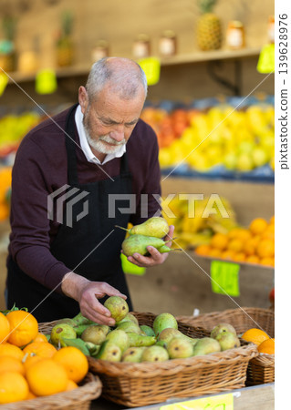Elderly owner of a farm shop stands near a fruit counter 139628976