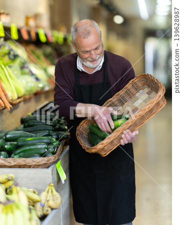 Elderly owner of a farm store holds a zucchini in hands Elderly owner of a farm store holds a zucchini in hands 139628987