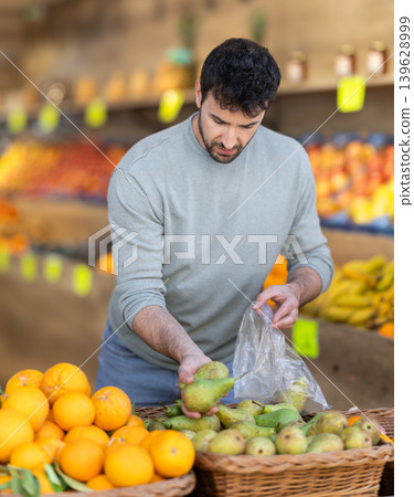 man carefully chooses pears to weigh them before buying man carefully chooses pears to weigh them before buying 139628999
