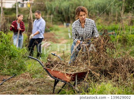 Woman takes out bunch of branches, puts garbage in wheelbarrow Woman takes out bunch of branches, puts garbage in wheelbarrow 139629002