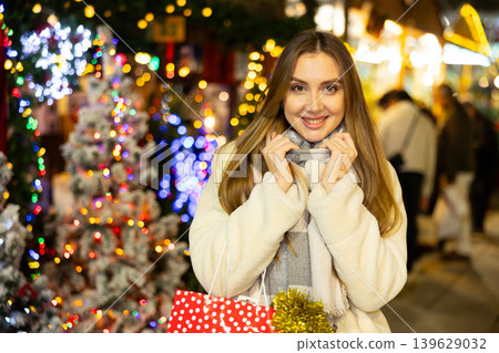 At Christmas outdoor market, girl with gift bag stands in center of crowded shopping area At Christmas outdoor market, girl with gift bag stands in center of crowded shopping area 139629032