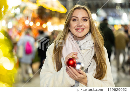 Portrait of dreamily happy girl with Christmas balls in her hands at a street fair in evening Portrait of dreamily happy girl with Christmas balls in her hands at a street fair in evening 139629062