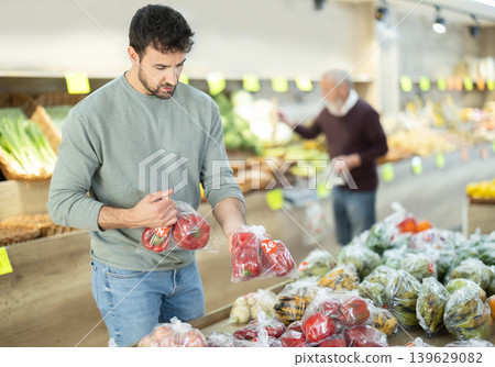 man stands in the vegetable section of a supermarket and chooses red bell peppers man stands in the vegetable section of a supermarket and chooses red bell peppers 139629082