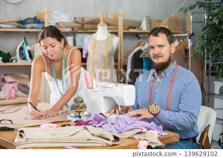 Male dressmaker sewing, girl draws with curves Male dressmaker sewing, girl draws with curves 139629102