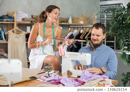 Flirty female colleague teasing shy male tailor Flirty female colleague teasing shy male tailor 139629154