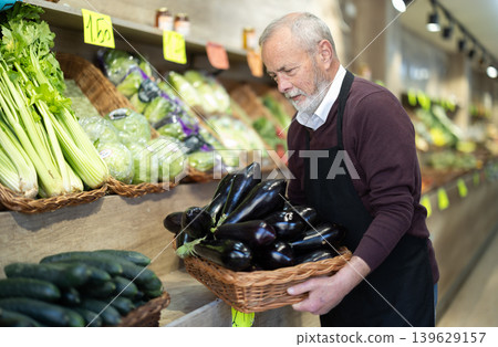 Elderly man seller puts eggplants in store Elderly man seller puts eggplants in store 139629157