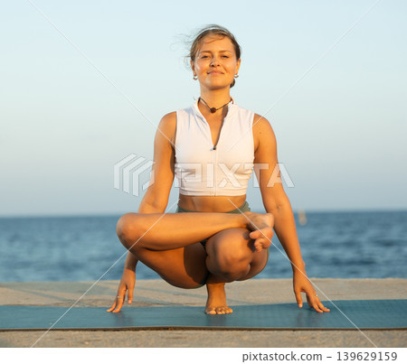 Woman in frog pose doing yoga on beach. Healthy lifestyle concept Woman in frog pose doing yoga on beach. Healthy lifestyle concept 139629159