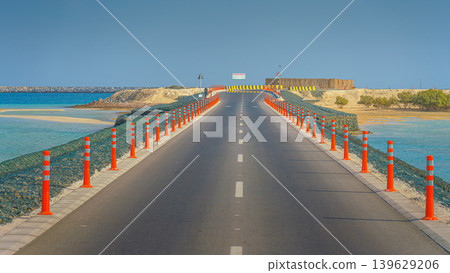 Sir Bani Yas Island, United Arab Emirates - Jan 18 2024, panoramic view of the road to the coast of the island, bordered by orange columns, no cars or people, Sir Bani Yas Island, UAE Sir Bani Yas Island, United Arab Emirates - Jan 18 2024, panoramic view of the road to the coast of the island, bordered by orange columns, no cars or people, Sir Bani Yas Island, UAE 139629206