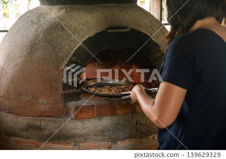 Someone bring a pizza into wood fired oven. It can also be used to dry and smoke food. Cooking on a wood fire is authentic and brings an unrivalled flavour to your dishes. Someone bring a pizza into wood fired oven. It can also be used to dry and smoke food. Cooking on a wood fire is authentic and brings an unrivalled flavour to your dishes. 139629329