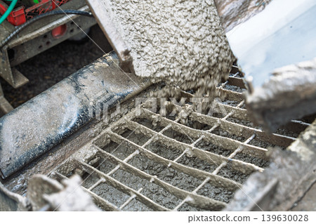 Pouring concrete from a mixer truck into a grate for construction and building projects Pouring concrete from a mixer truck into a grate for construction and building projects 139630028