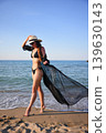 Woman walking by the sea in black bikini with sheer flowing cover up 139630143