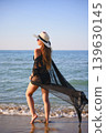 Back view of woman walking on beach in black bikini with sheer cover up 139630145