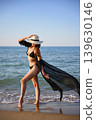 Woman walking at shoreline in black bikini with flowing sheer cover up 139630146