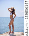 Woman posing on seaside rocks in bikini and sun hat in summer 139630147