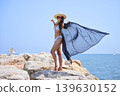 Woman in bikini with flowing cover up on seaside rocks in summer 139630152