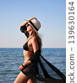 Side profile of woman in black bikini with sheer cover up by the sea 139630164