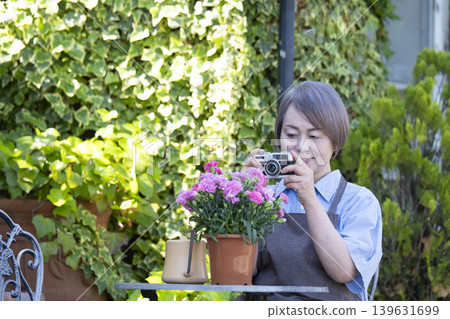 一位老婦人在自家院子裡侍弄花草時，正在拍攝花朵的照片。 139631699