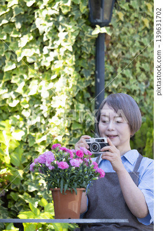 一位老婦人在自家院子裡侍弄花草時,正在拍攝花朵的照片。 一位老婦人在自家院子裡侍弄花草時,正在拍攝花朵的照片。 139631702