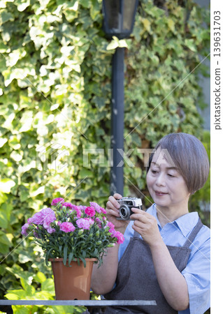 一位老婦人在自家院子裡侍弄花草時，正在拍攝花朵的照片。 139631703